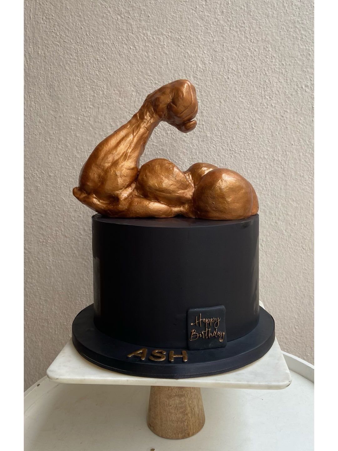 Black birthday cake topped with a metallic gold sculpted flexing muscle arm.