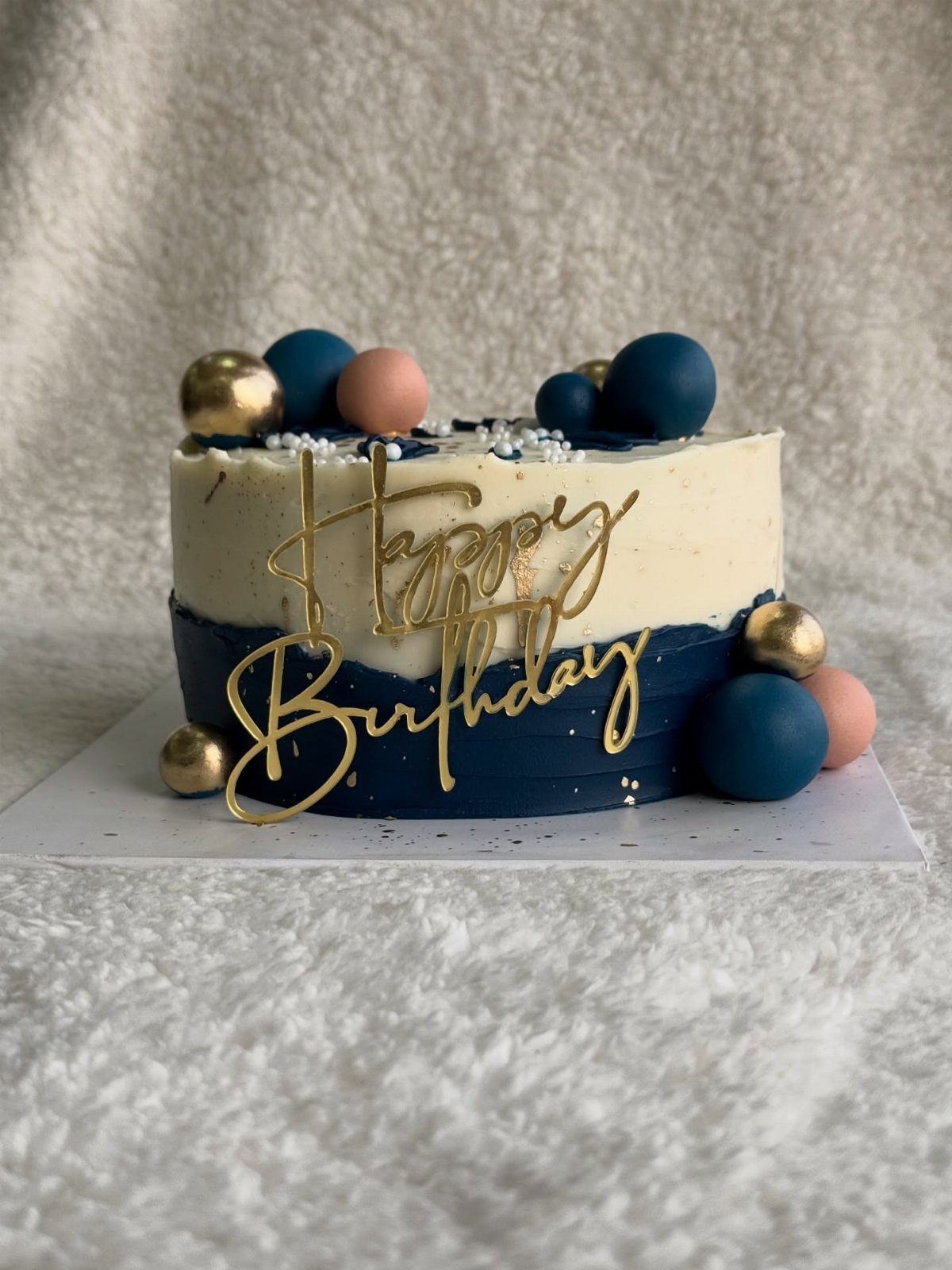 Navy blue and white frosted cake with gold spheres and Happy Birthday topper.