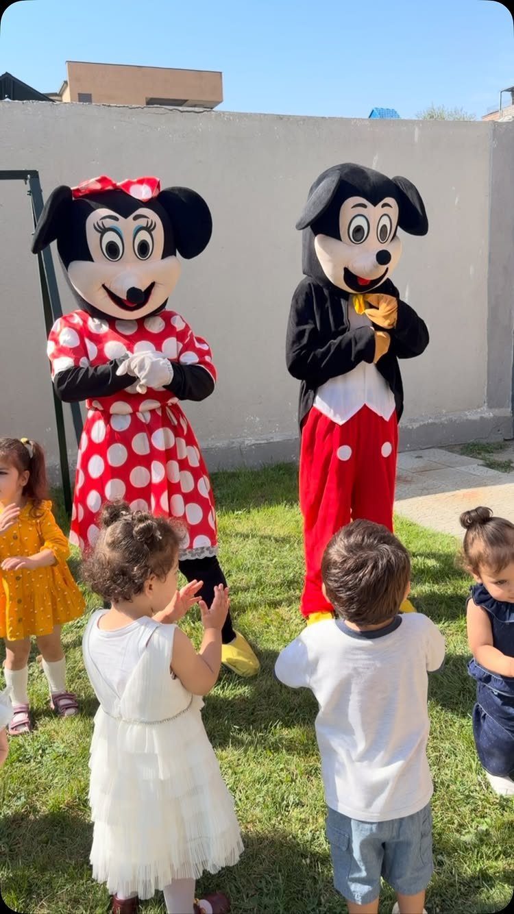 Mickey and Minnie Mouse characters interacting with young children on a sunny lawn.