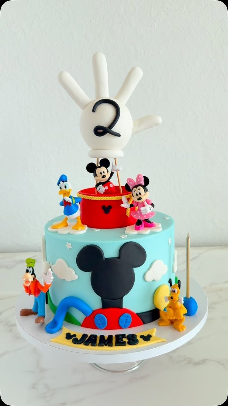 Mickey Mouse themed birthday cake with character figurines and a number two balloon.