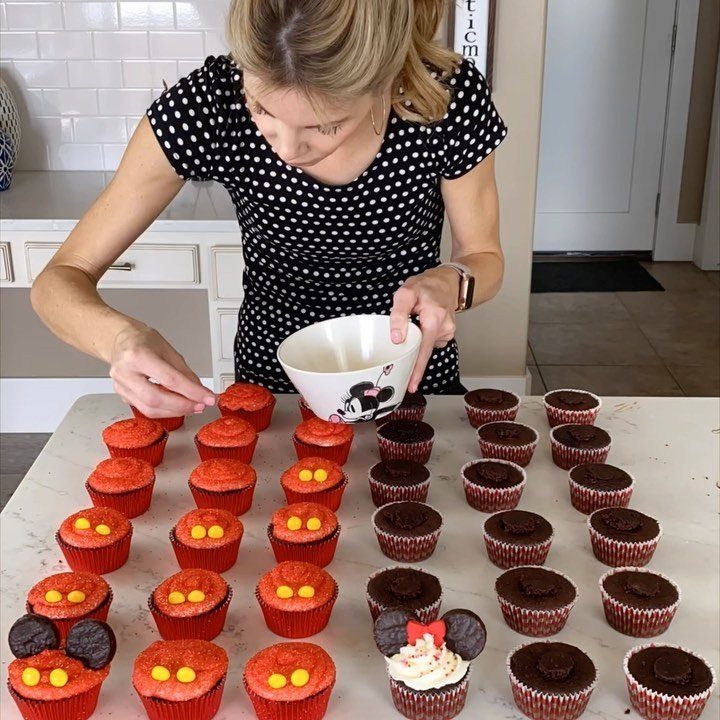Woman decorating red and chocolate Mickey Mouse themed cupcakes on a white counter