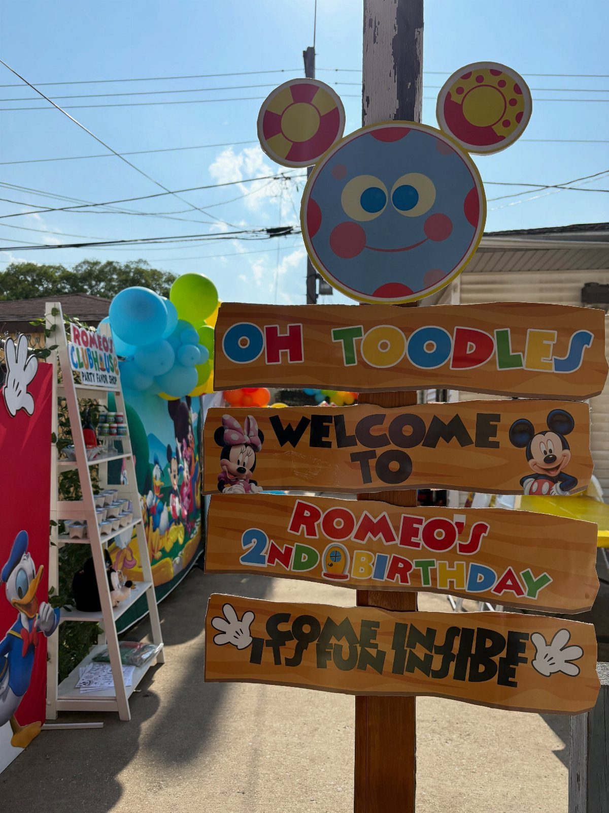 Wooden Mickey Mouse welcome sign for a second birthday party with colorful balloons.
