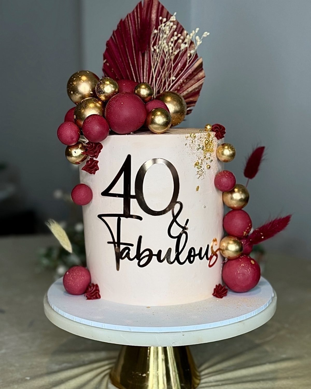 Light pink 40th birthday cake with burgundy spheres and 40 and Fabulous topper