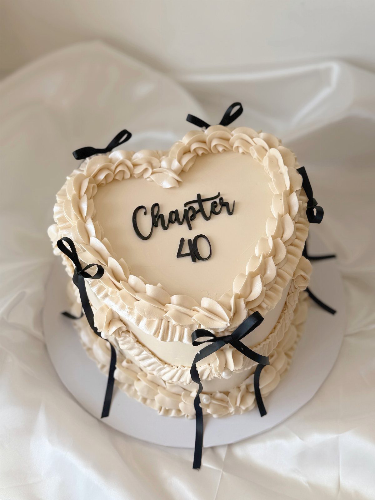 Heart-shaped cream cake with ruffled frosting, black bows, and Chapter 40 text.