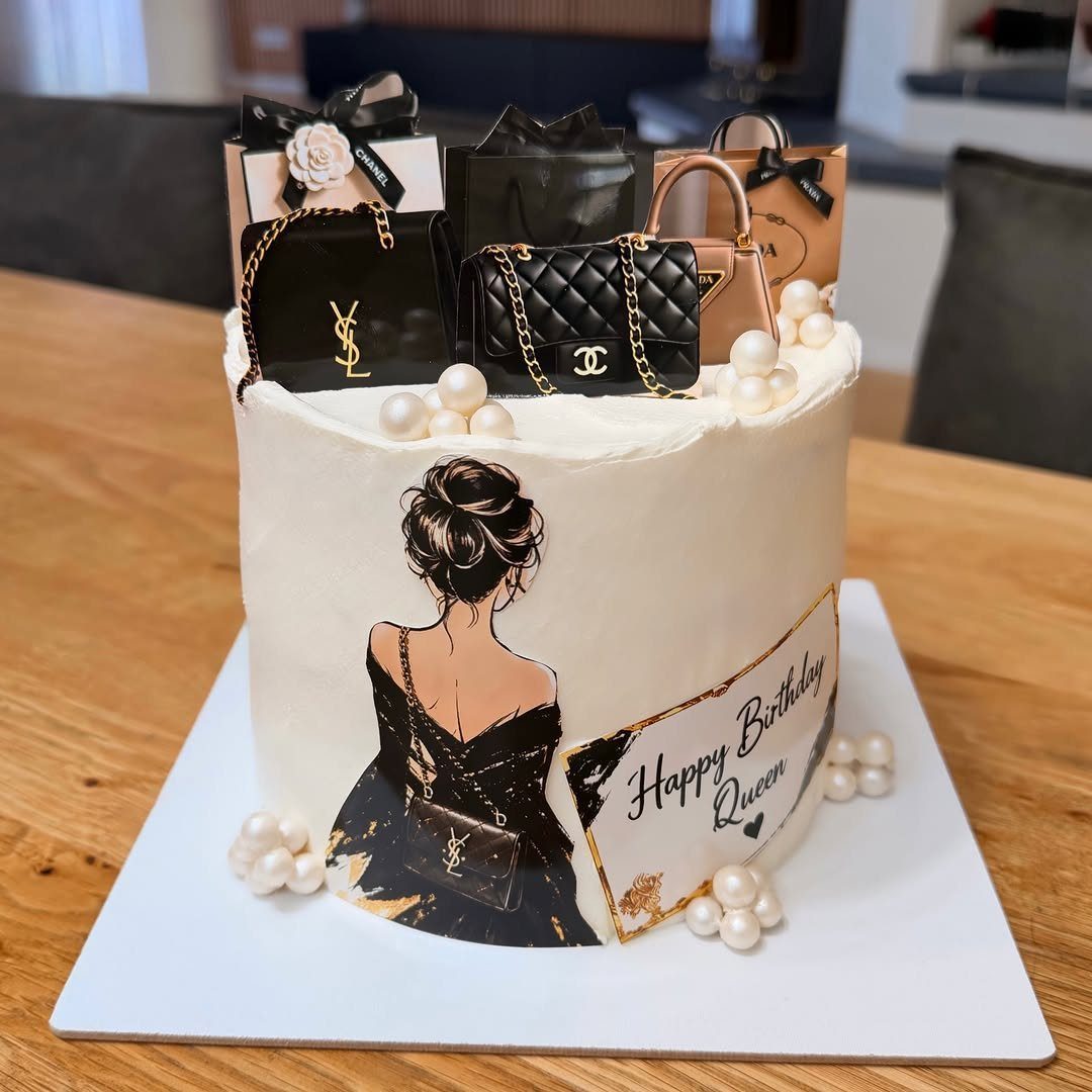 White birthday cake decorated with luxury handbag miniatures, pearls, and a woman's silhouette.