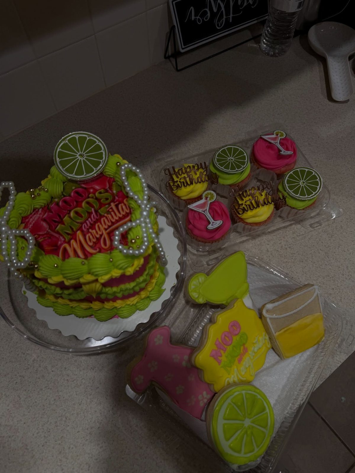 Green and pink margarita themed cake with lime slices, cupcakes, and cookies.