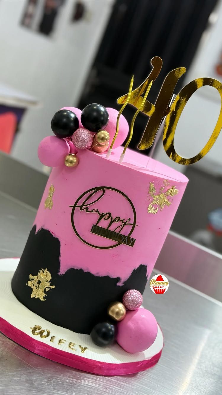 Pink and black 40th birthday cake with gold topper and decorative spheres.