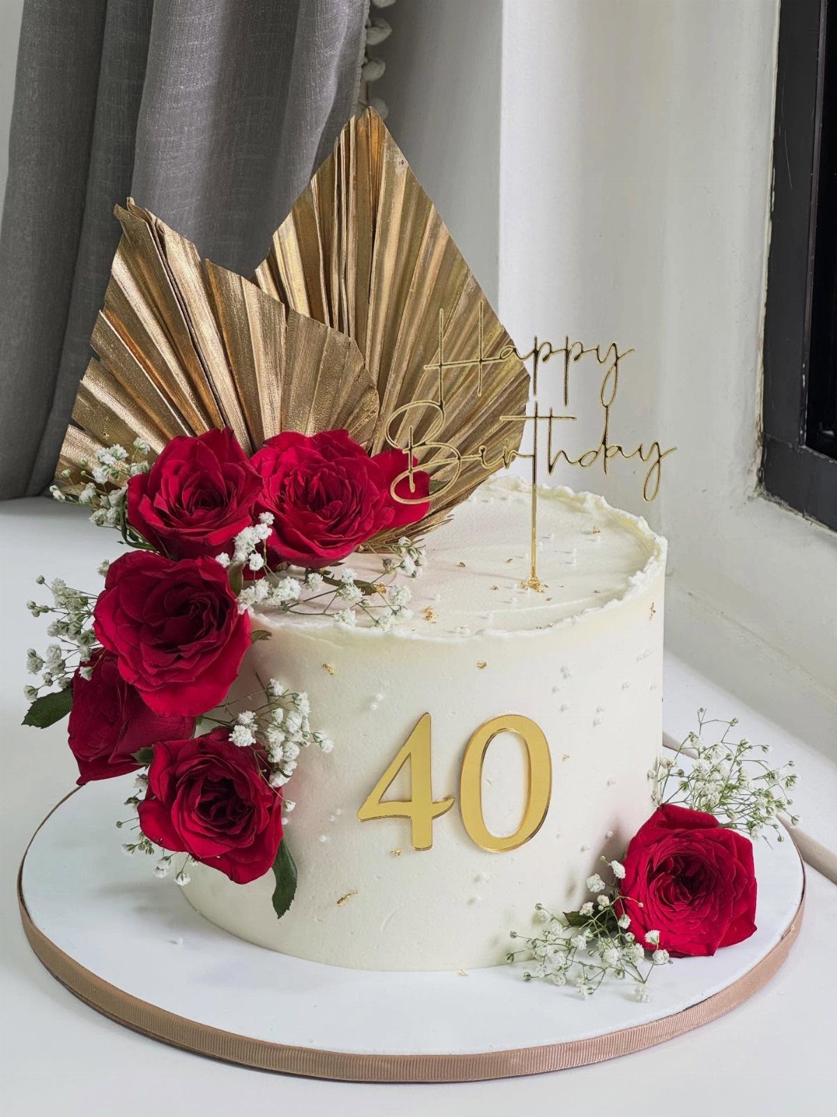 White birthday cake with red roses, gold number 40, and gold fan toppers.