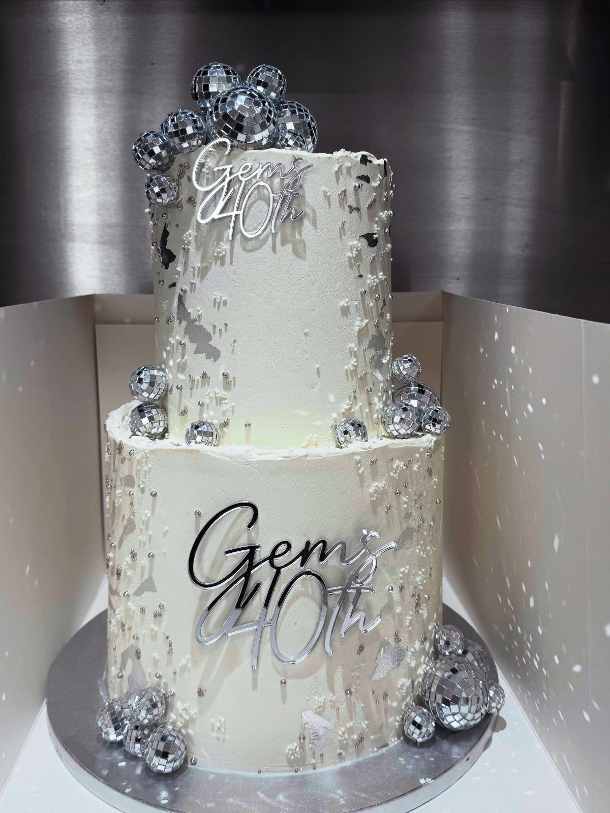 Two-tier white birthday cake with silver splatters, disco balls, and 40th topper.