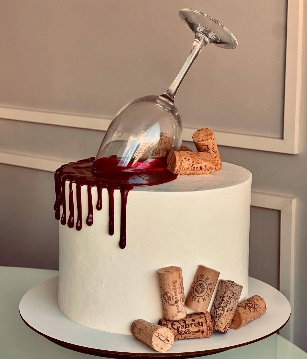 White frosted cake with a tipped wine glass spilling red syrup and corks.