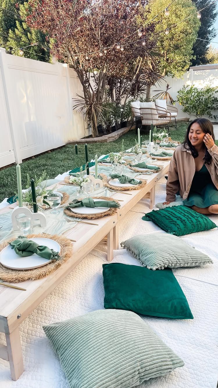 Low wooden party table with green decor and cushions on a backyard lawn