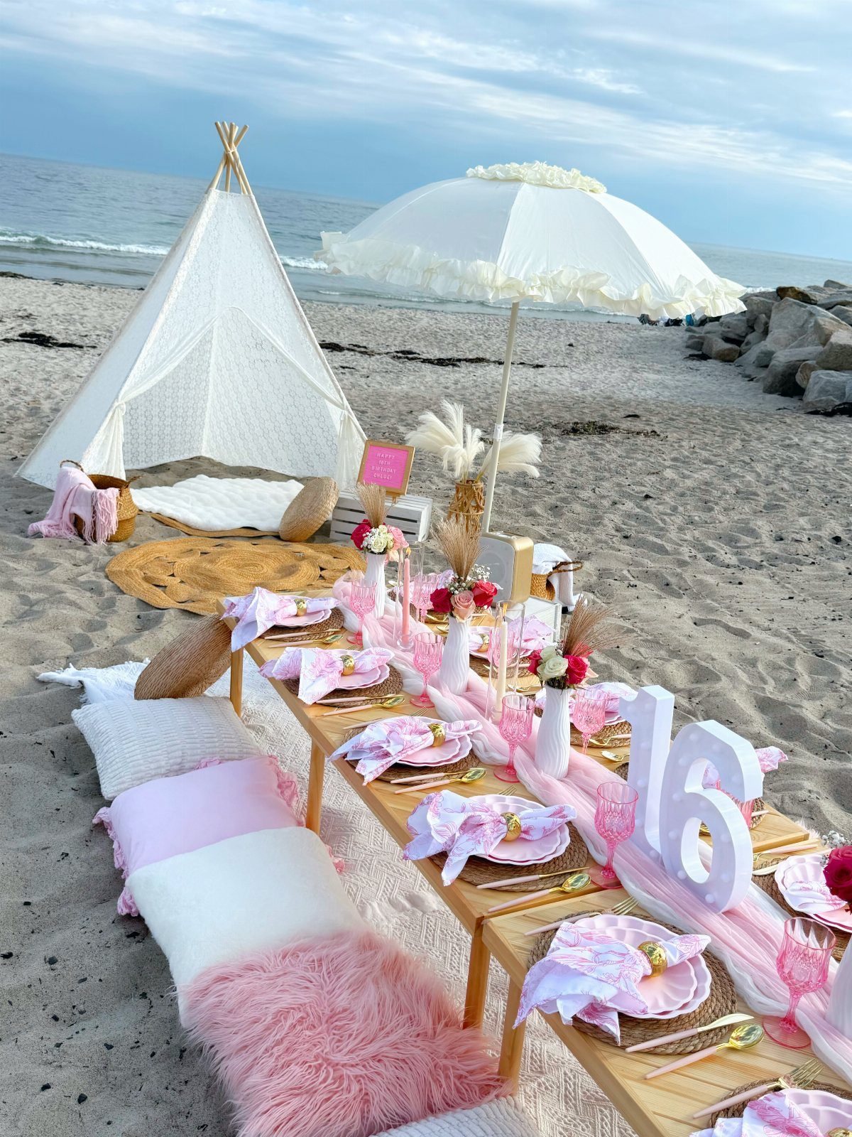 Beach party setup with pink decorations, a white teepee, and a long table.