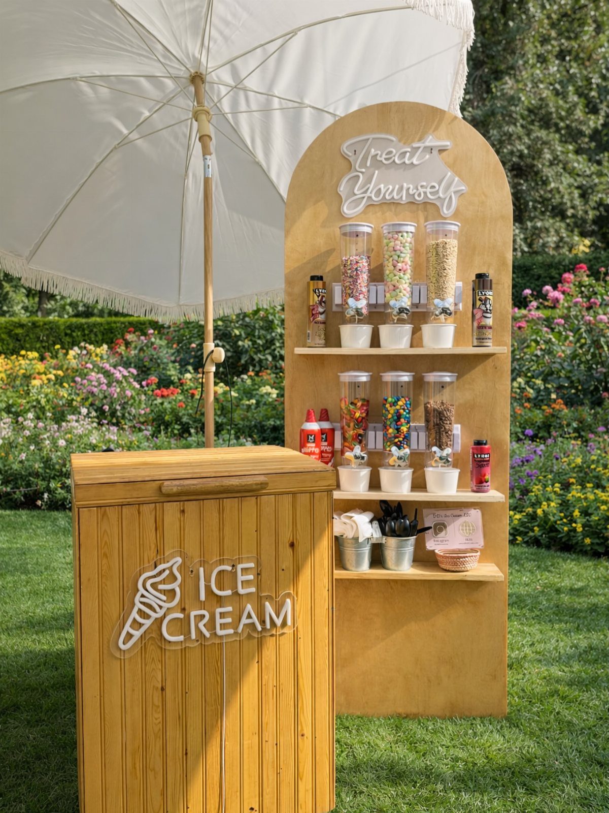 Ice cream station with wooden chest and topping bar under a white umbrella.