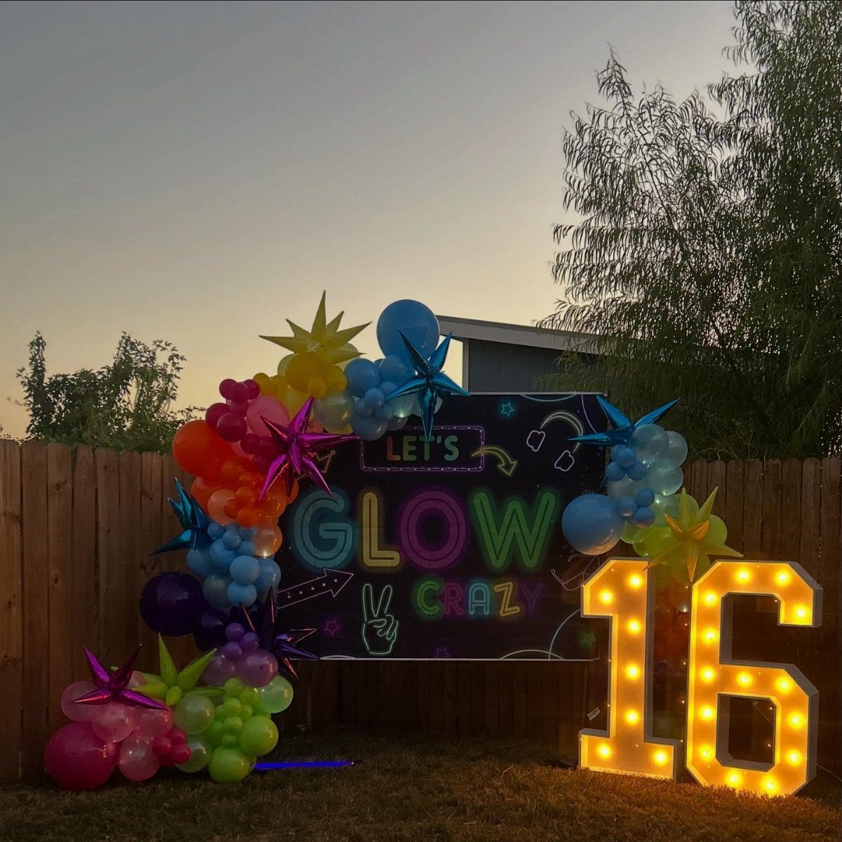 Colorful balloon arch and glowing marquee number 16 for an outdoor birthday party.