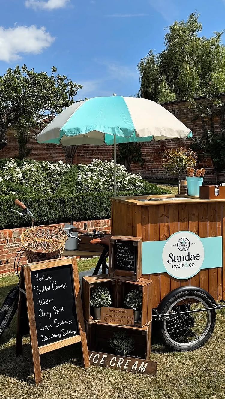 Wooden ice cream cart with blue and white umbrella on a sunny lawn
