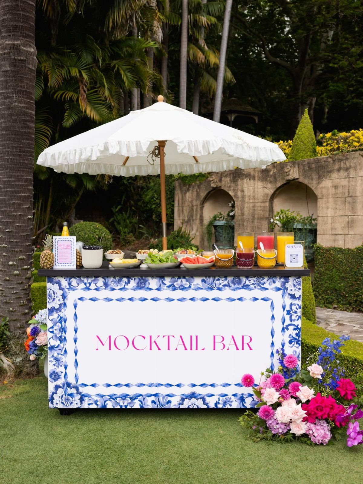 Mocktail bar with blue and white patterns, colorful drinks, and a white umbrella.