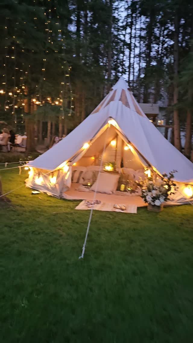 White bell tent with warm interior lighting on a grassy lawn among trees