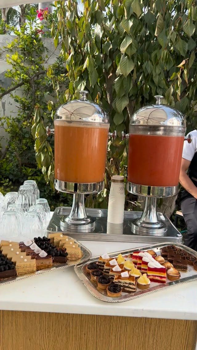 Beverage dispensers and dessert trays on a white table at an outdoor party.
