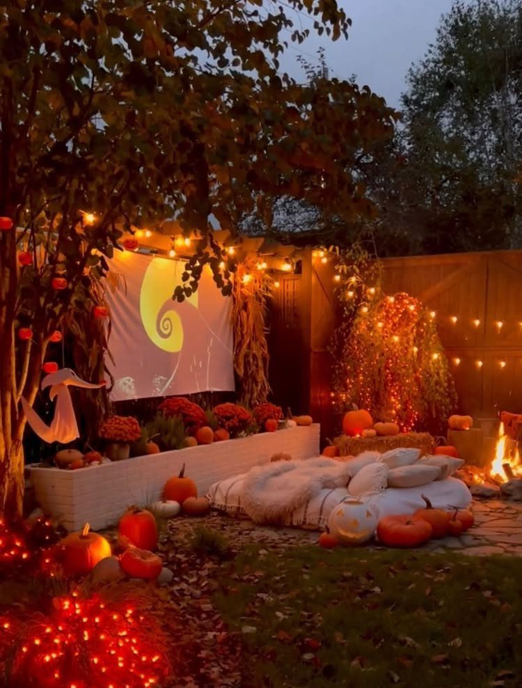 Outdoor movie screen with pumpkins, cozy blankets, and string lights in a backyard.