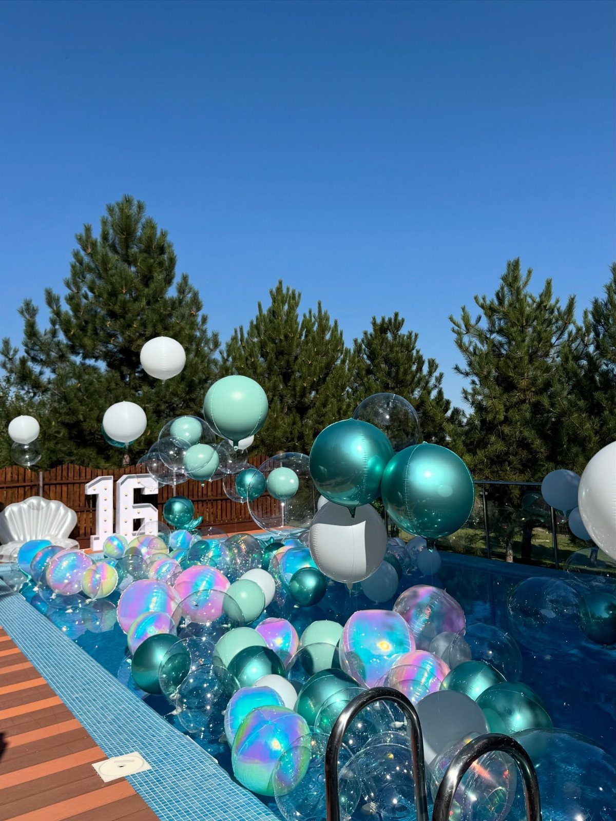 Swimming pool filled with iridescent balloons and large white number 16 decorations.