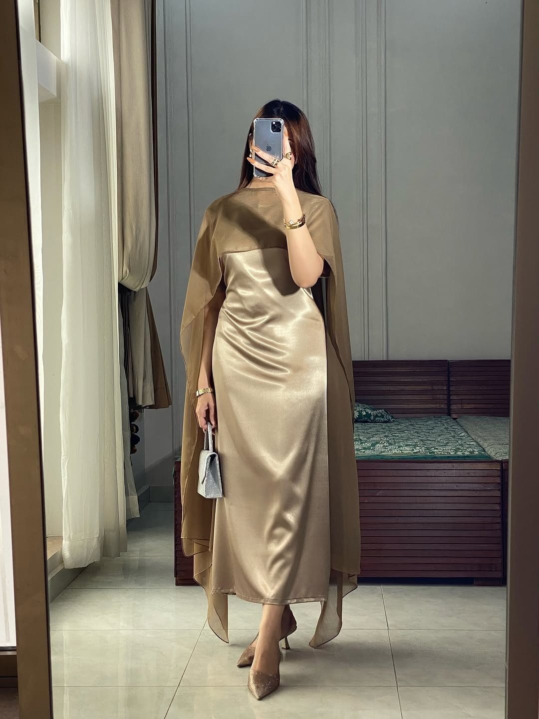 Woman in champagne satin slip dress with a matching sheer cape and nude heels.