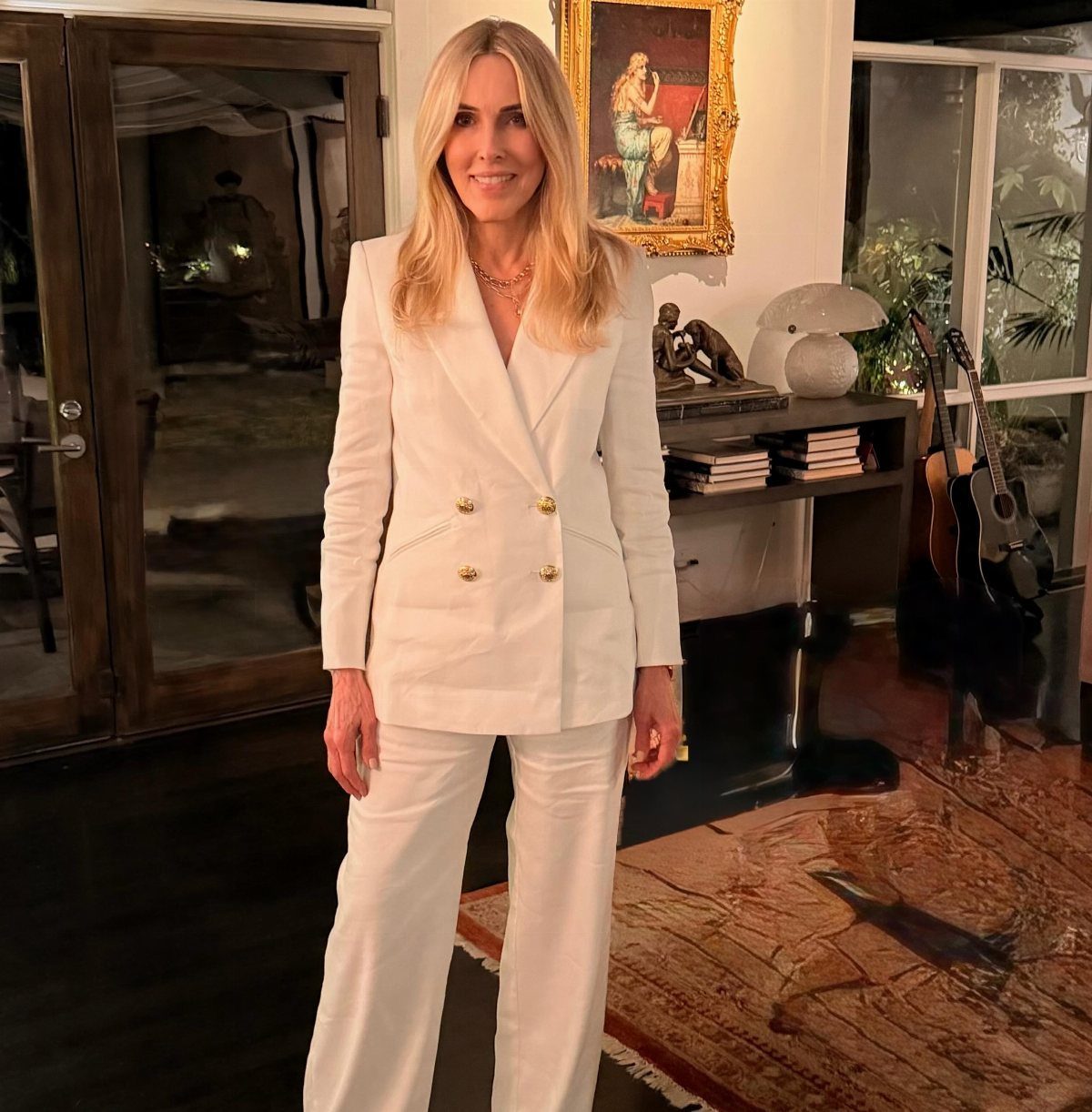 Woman wearing a tailored white double-breasted suit with wide-leg trousers in a home.
