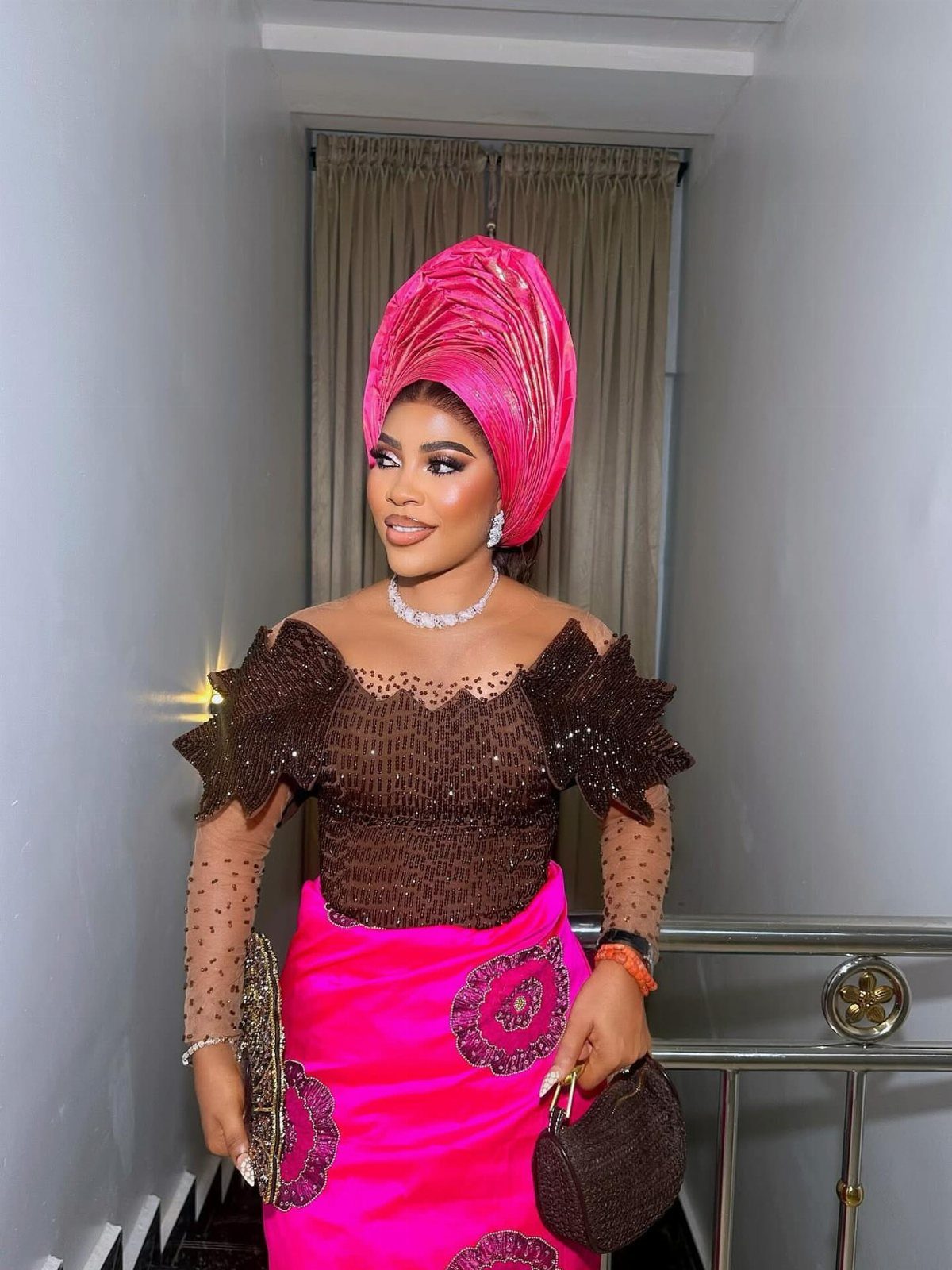 Woman in a pink headwrap, brown beaded top, and pink patterned skirt.