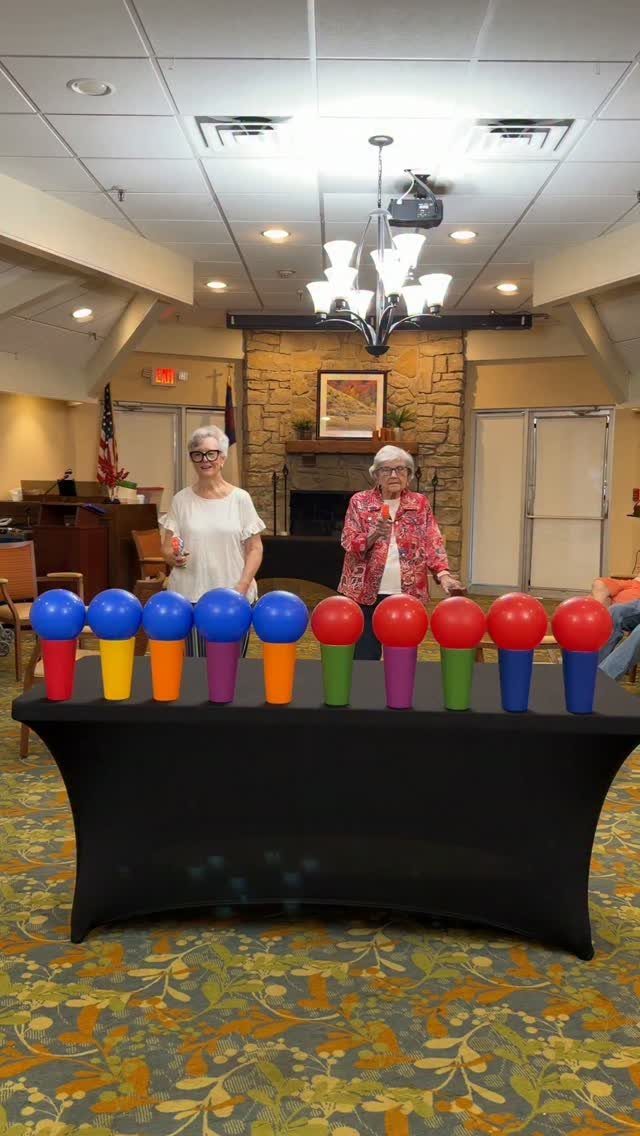 Two elderly women standing behind a table with colorful balloons on cones.