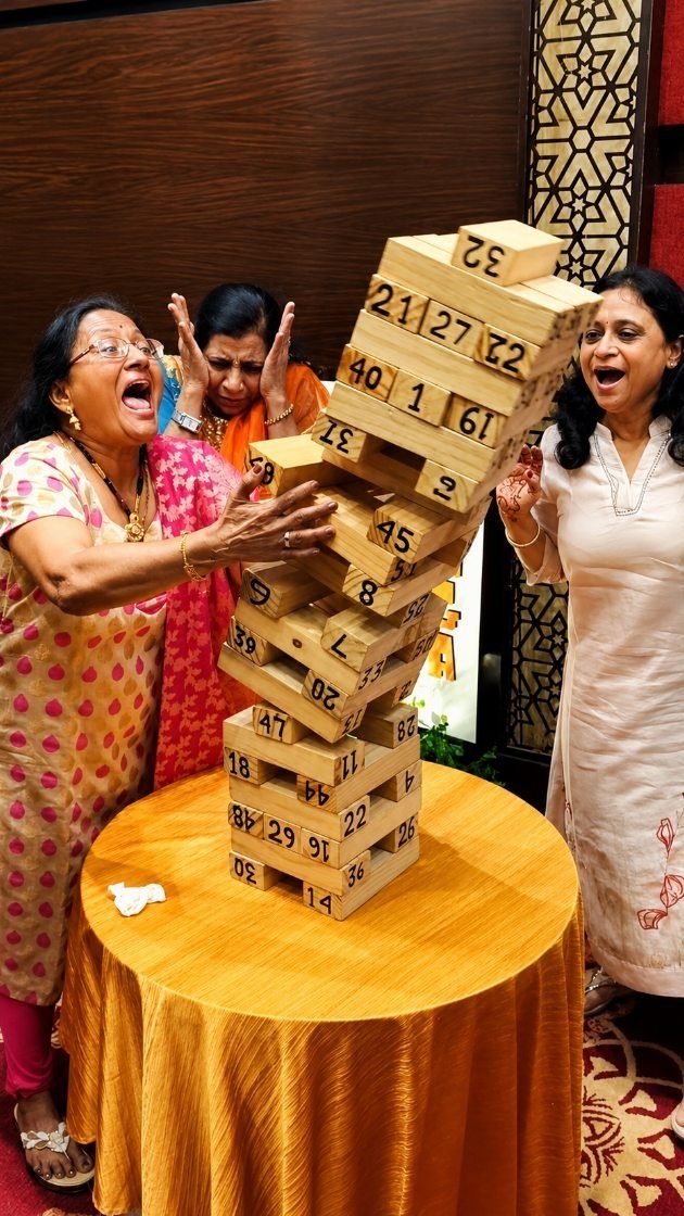Three women reacting as a tower of numbered wooden blocks falls over.