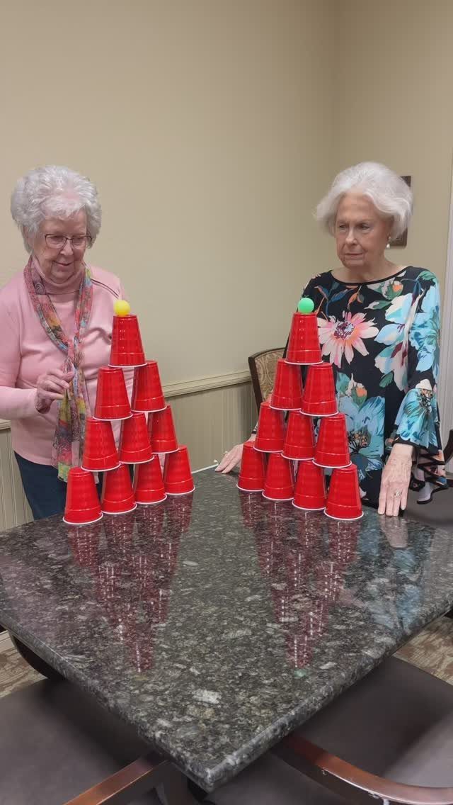 Two elderly women standing by red plastic cup pyramids on a granite table.