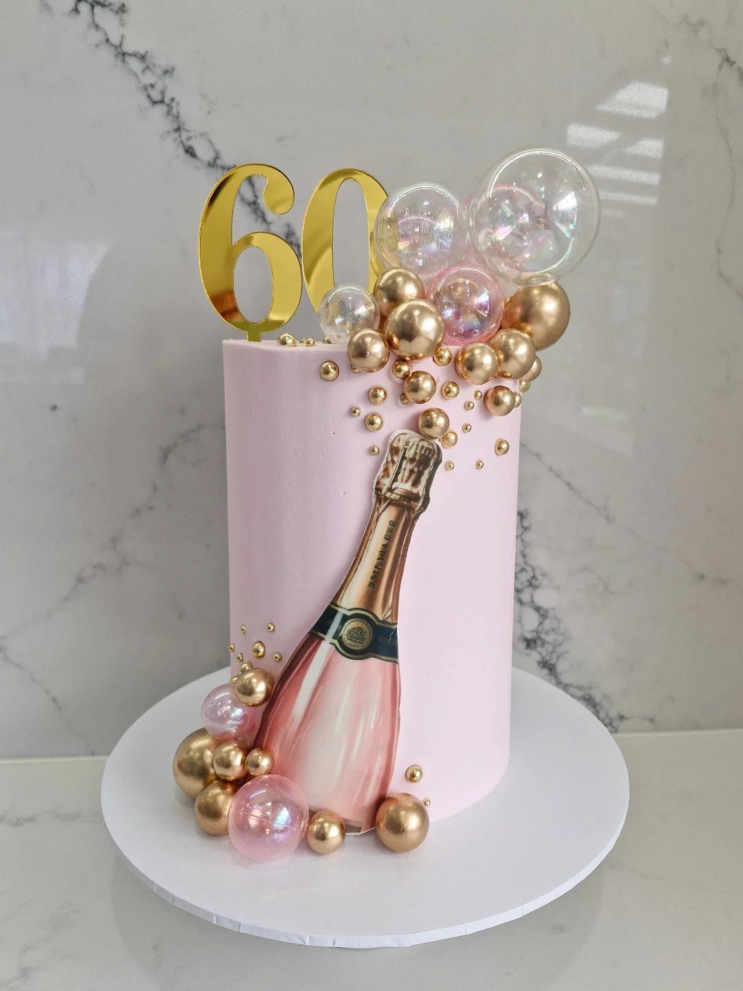 Pink birthday cake with a champagne bottle decoration and gold 60 topper
