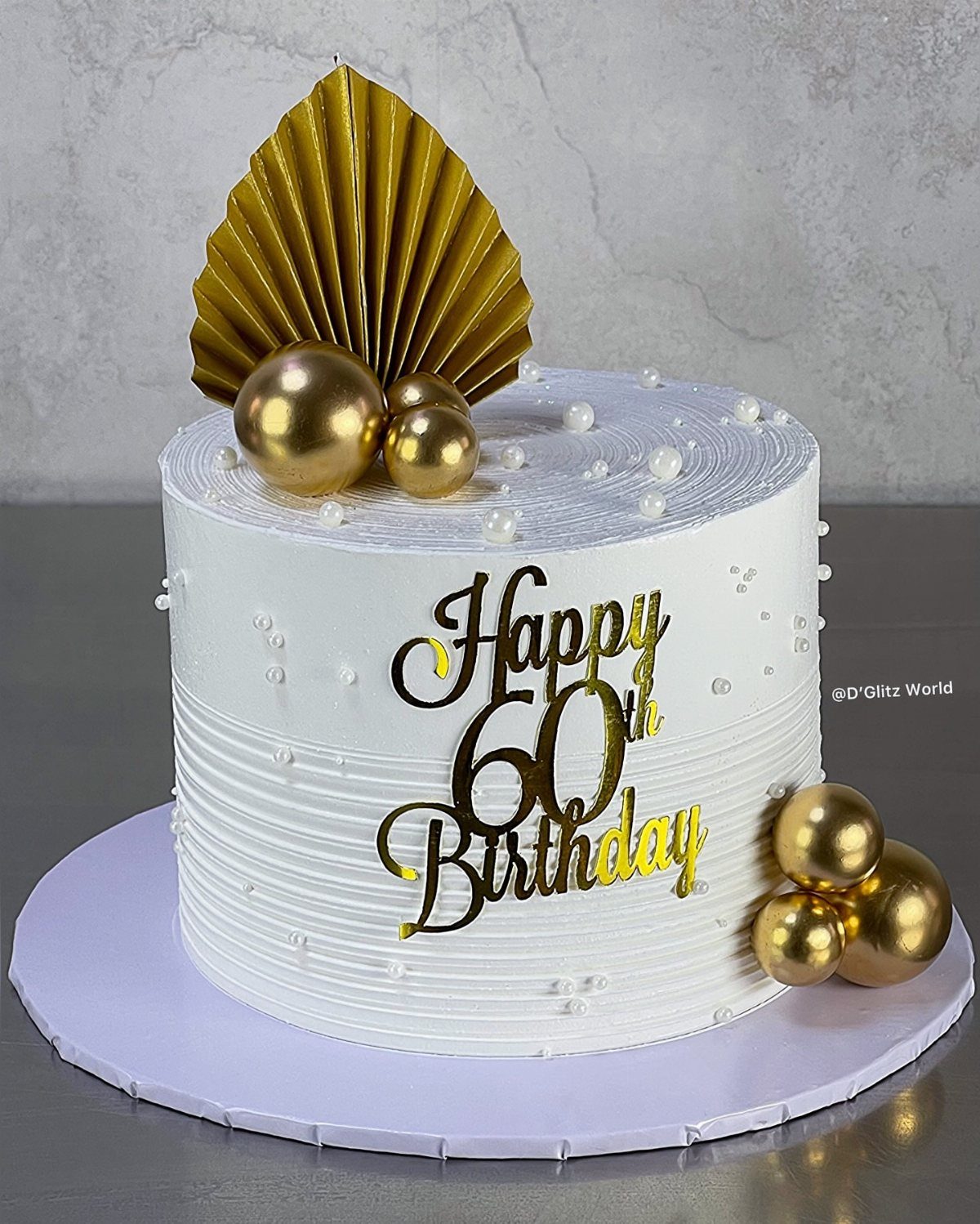 White buttercream cake with gold spheres and a Happy 60th Birthday topper.