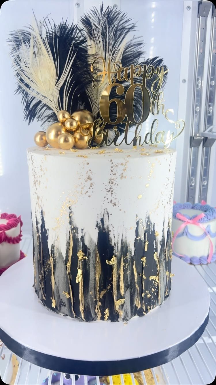 White and black cake with gold accents, feathers, and 60th birthday topper.