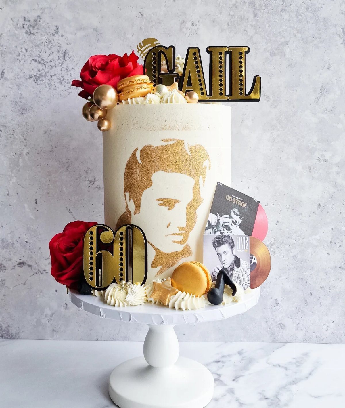 White birthday cake with gold Elvis silhouette, red roses, and gold 60 topper.