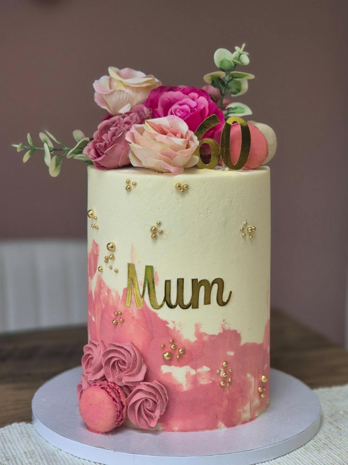 White cake with pink watercolor frosting, topped with roses and gold 60 topper.