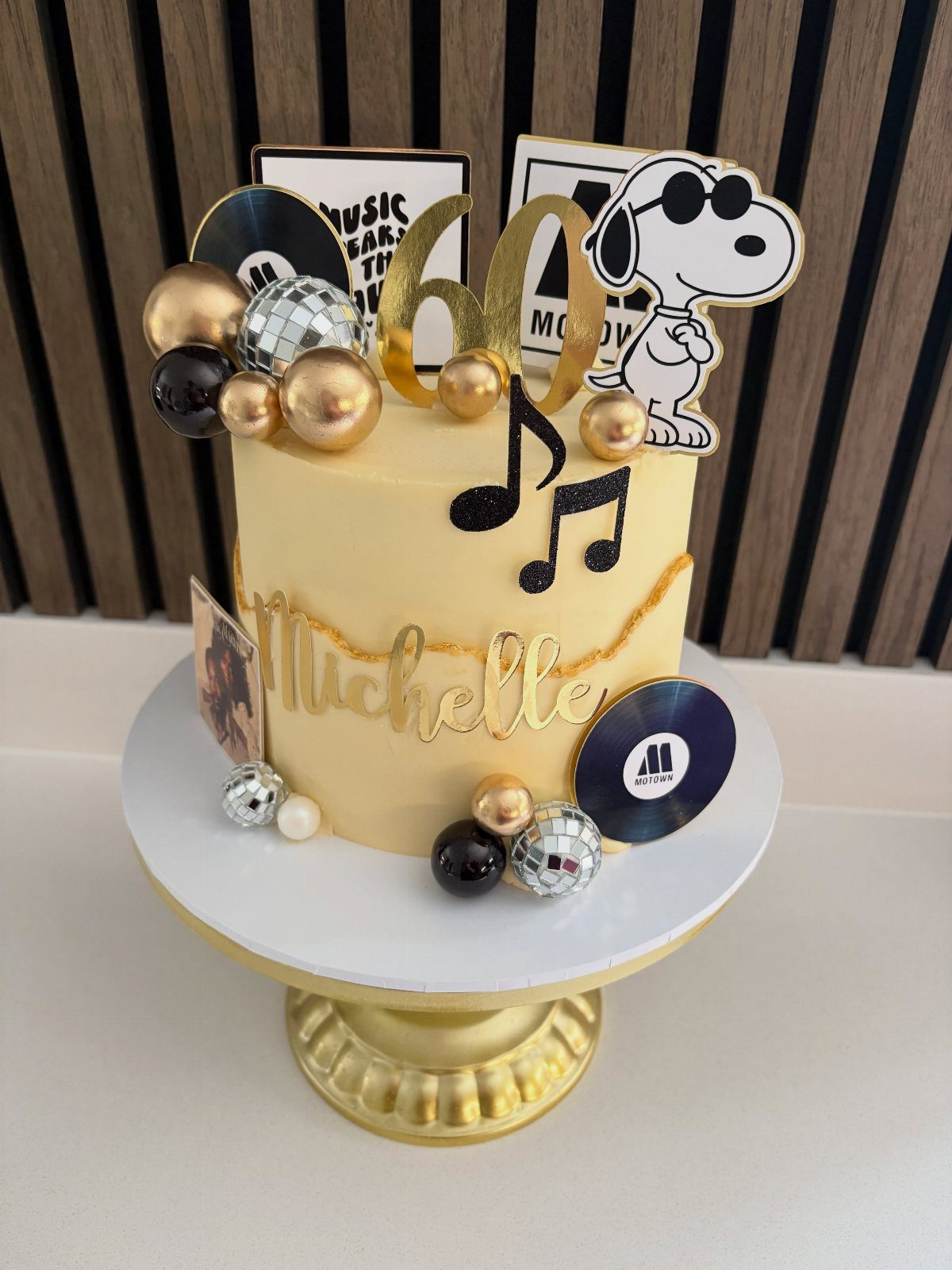 Yellow 60th birthday cake decorated with musical notes, vinyl records, and Snoopy topper.