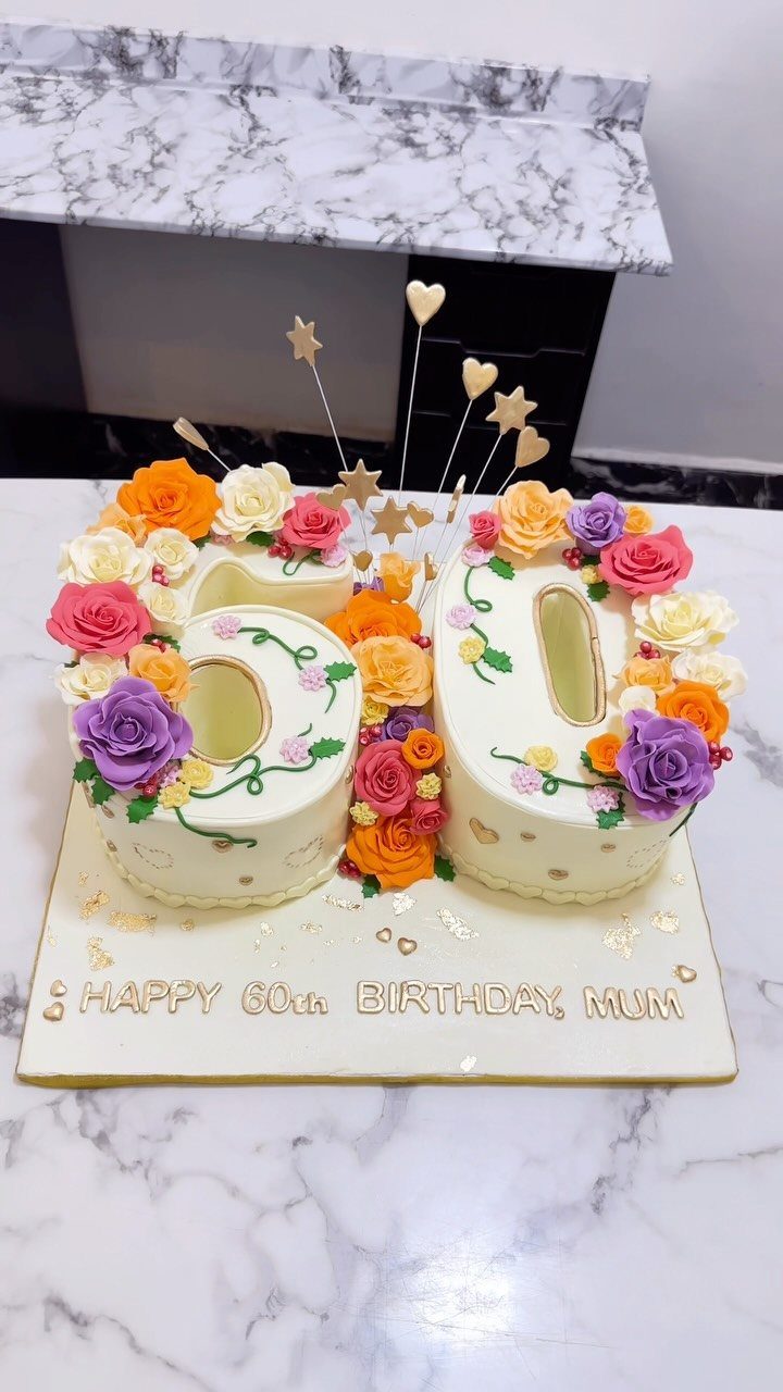 Number 60 shaped cake decorated with colorful frosting roses and gold birthday lettering.
