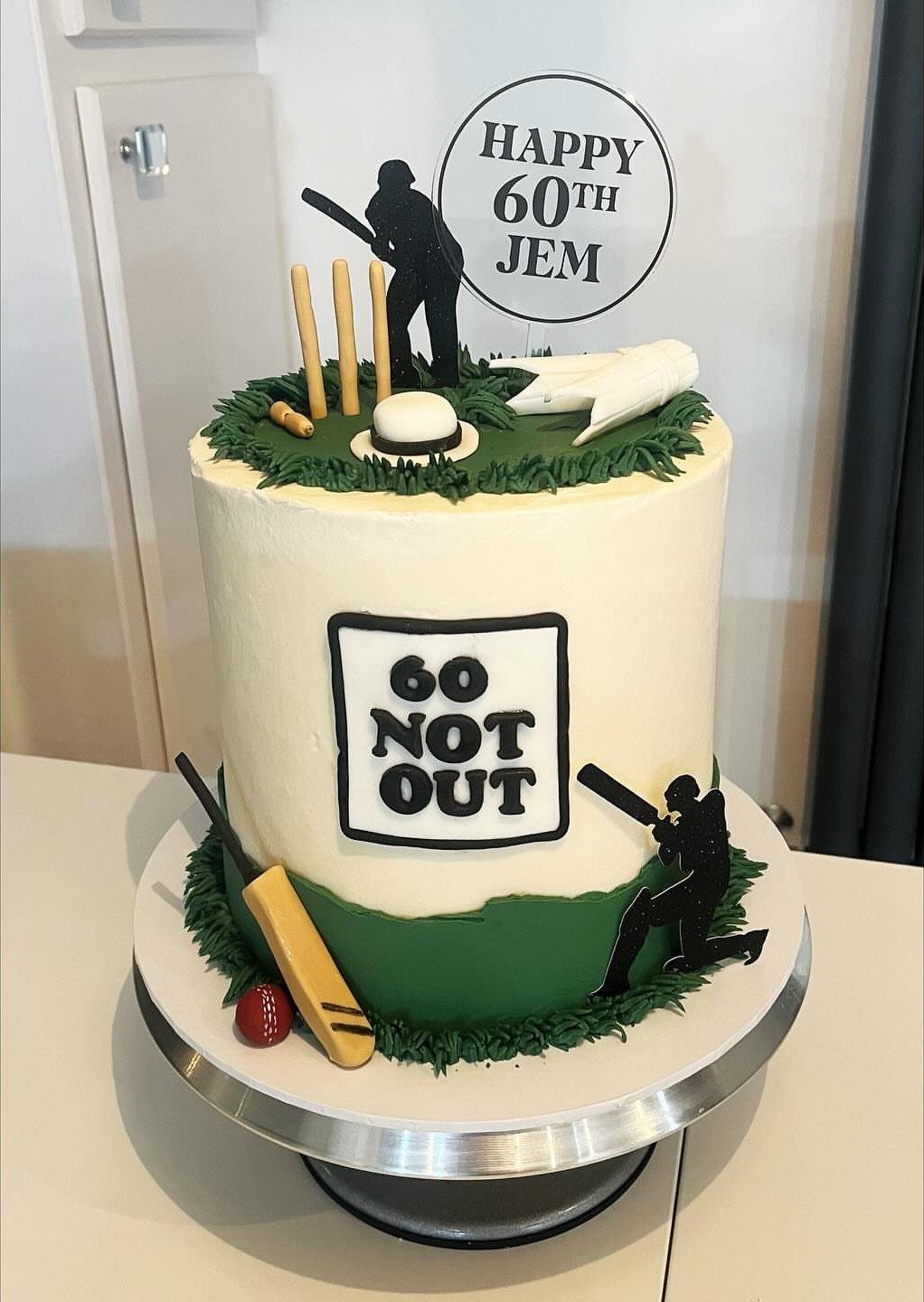 Cricket themed 60th birthday cake with players, bat, ball, and grass decorations.