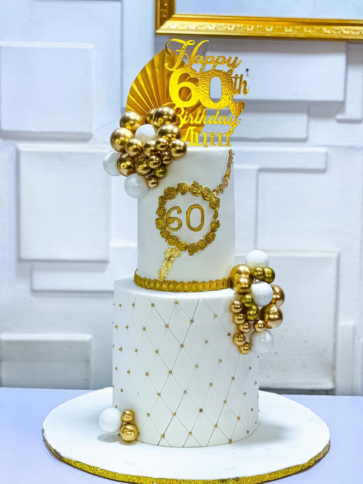 Two-tier white birthday cake with gold quilted pattern and 60th birthday topper.