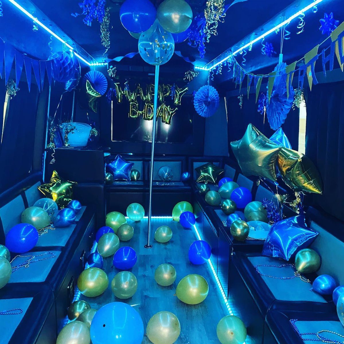 Luxury party bus interior decorated with blue neon lights and gold birthday balloons.