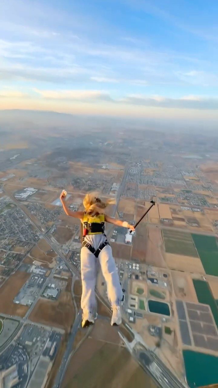 Woman skydiving over a rural landscape with fields and buildings under a blue sky