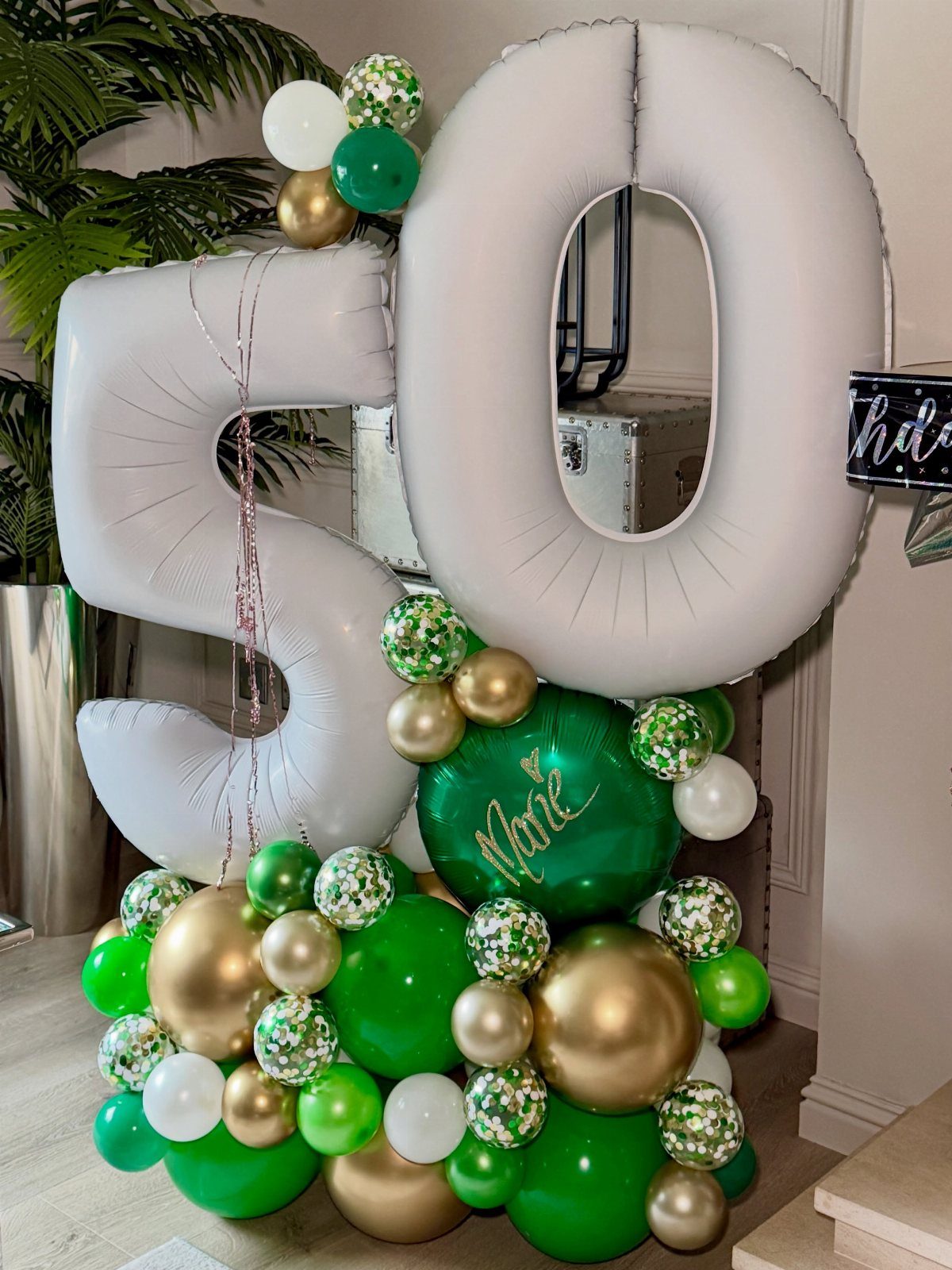 White inflatable number 50 balloons resting on a cluster of green and gold balloons.