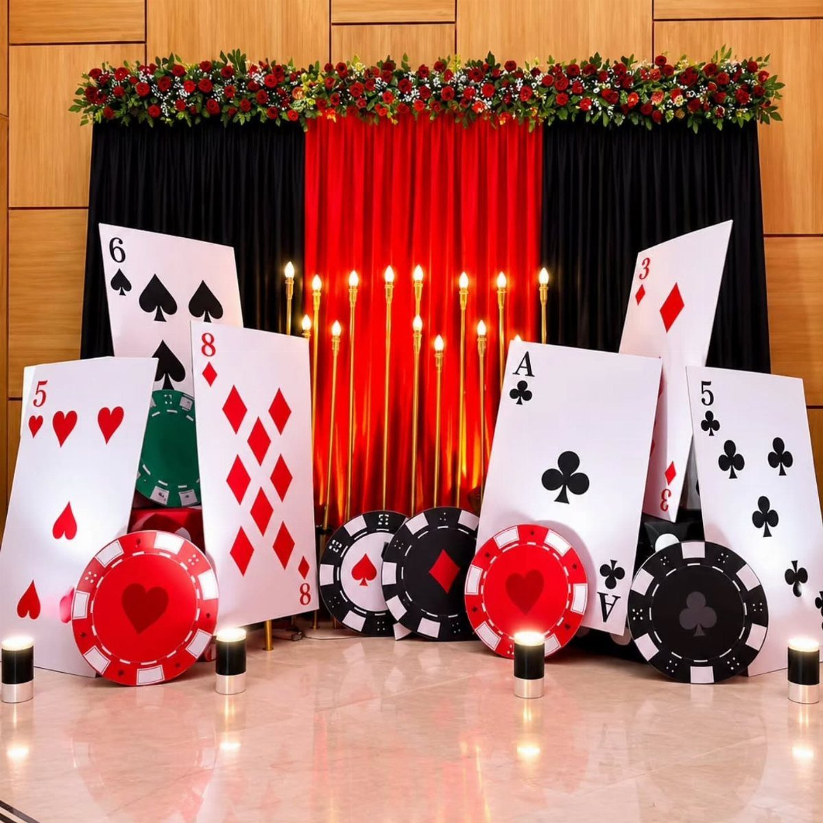 Oversized playing cards and poker chips arranged before red and black curtains.