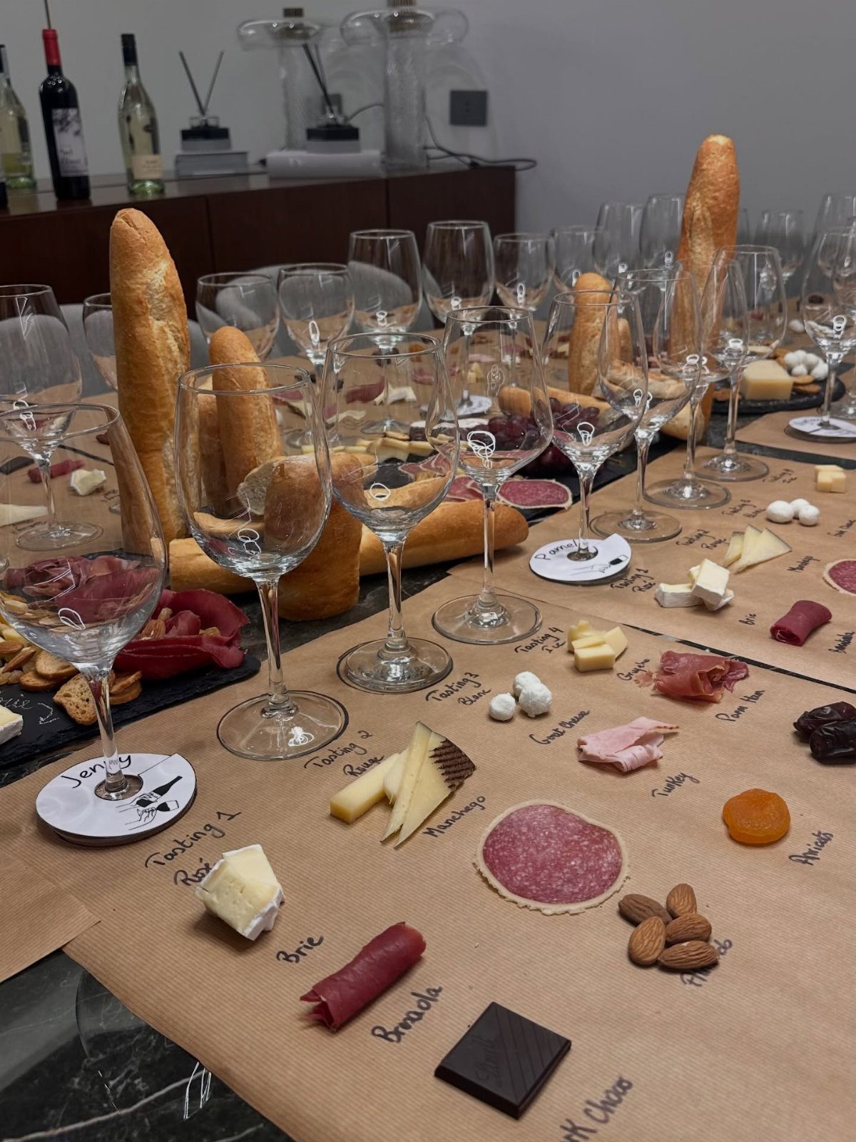Charcuterie spread with baguettes, cheeses, and wine glasses on a brown paper table.