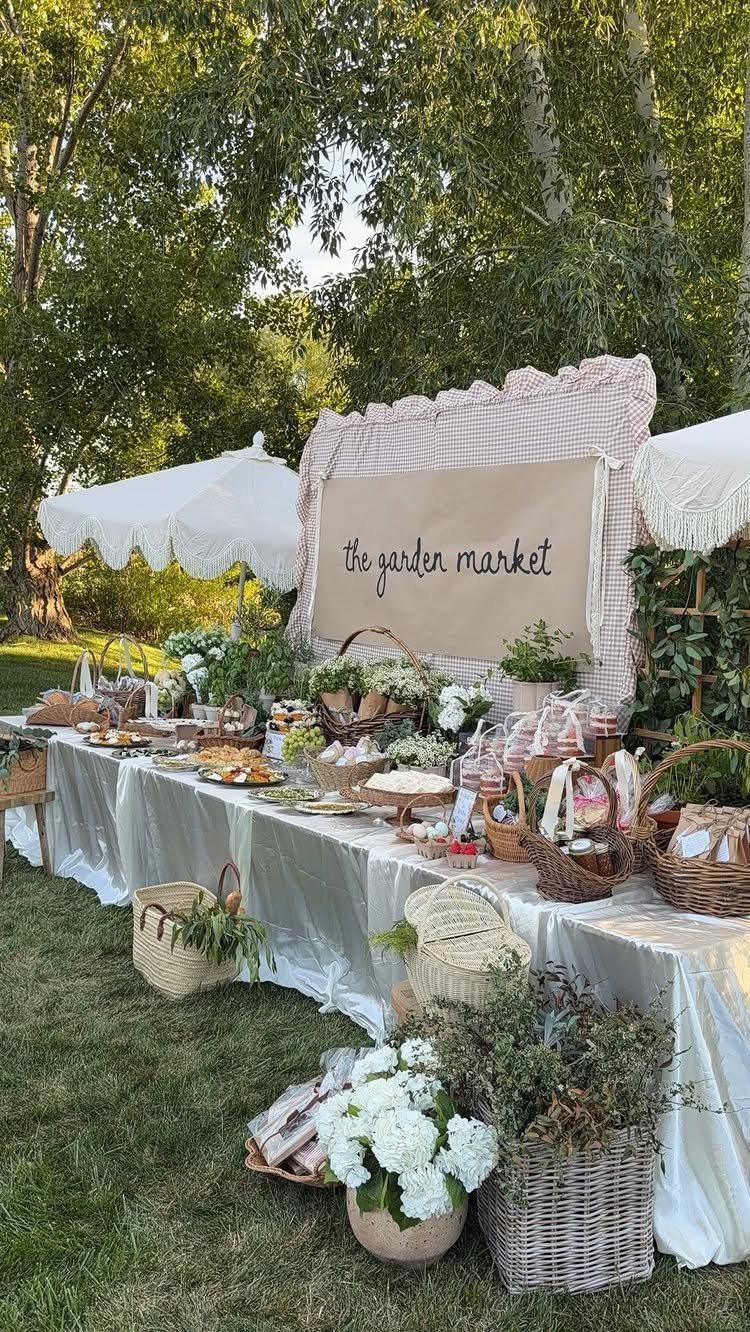 Outdoor garden market food display with white tablecloth, baskets, and floral arrangements.