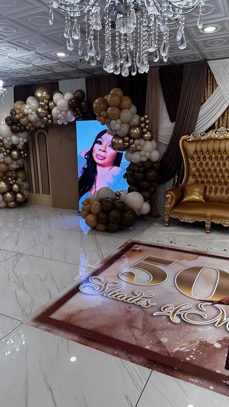 Luxurious 50th birthday party setup with gold balloons, throne chair, and custom floor decal.