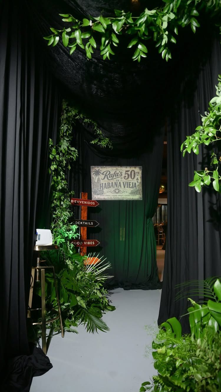 Tropical party entrance with black curtains, green plants, and Havana themed signage.