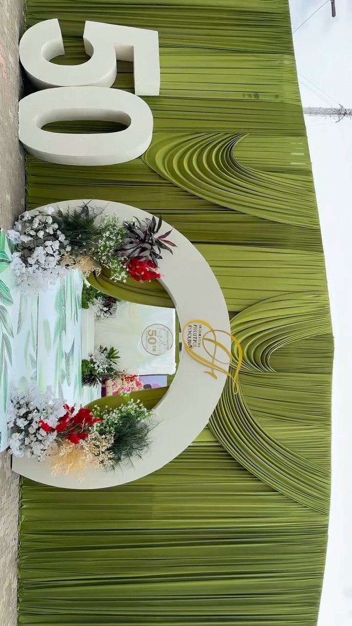Green pleated backdrop with large white 50 numbers and a circular floral arrangement.