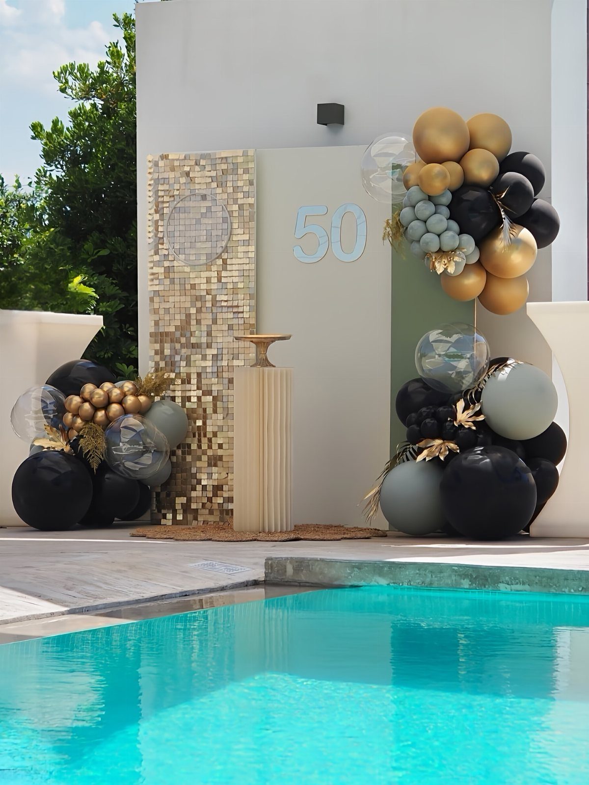 Poolside party decorations with gold and black balloons and a number 50 sign.
