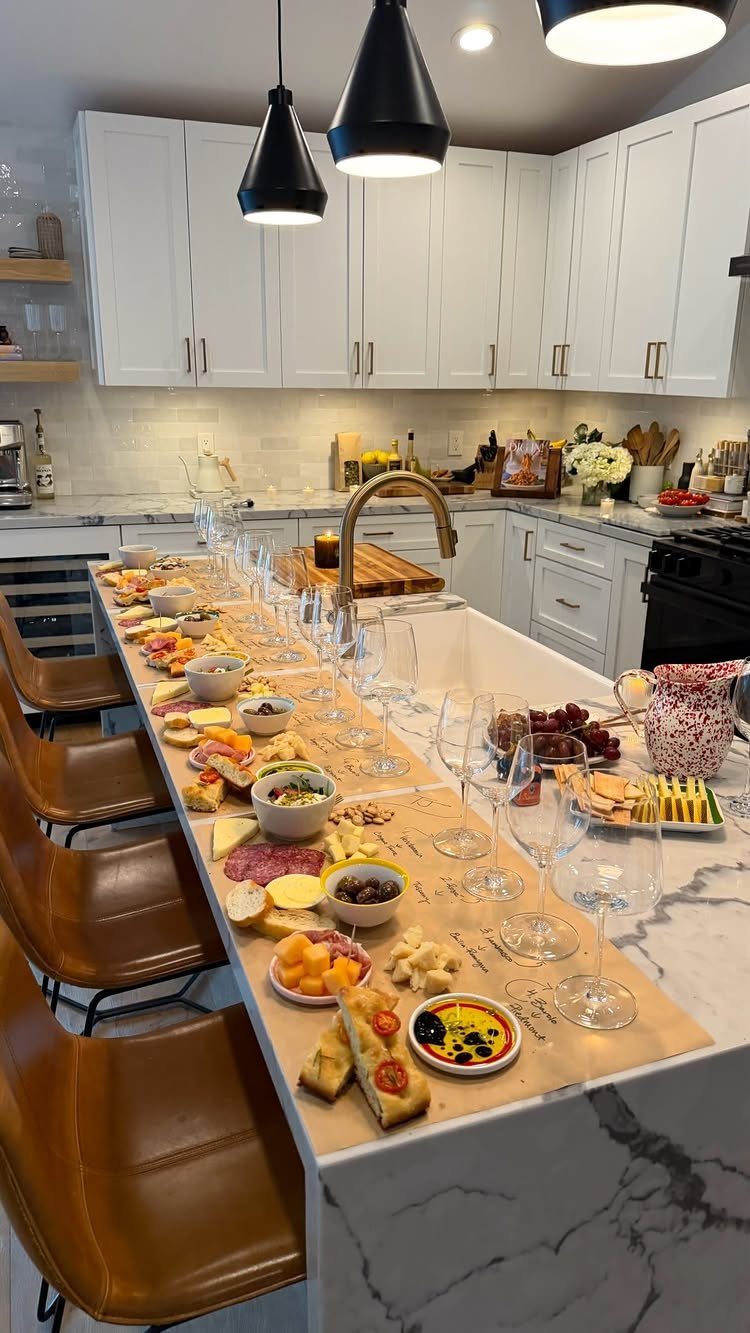 Wine and cheese spread with glasses arranged on a modern kitchen island.